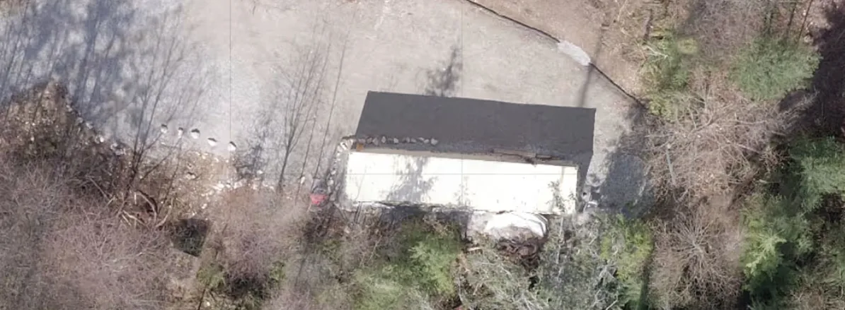 Drone view of an existing building and cleared yard on a forested lot